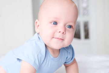 portrait of smiling baby boy with big blue eyes in bodysuit on white bedding. Healthy newborn child