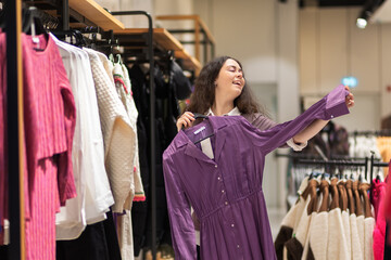 Young happy Caucasian woman tries on purple dress in shop. Buying of dreams. Cocept of shopping and...