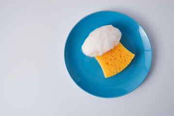 Yellow soapy sponge with foam on blue plate. Cleaning concept. Copy space