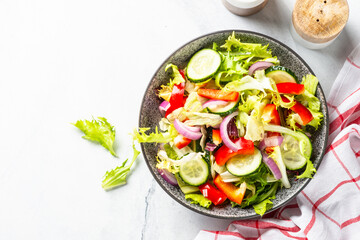Vegan salad with green leaves, cucumber and bell pepper on white. Top view with copy space.