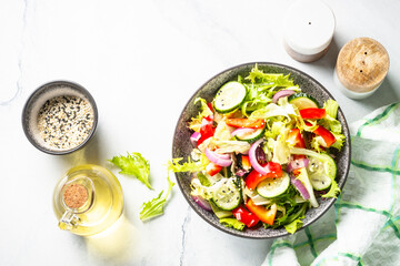 Vegan salad with green leaves, cucumber and bell pepper on white. Top view with copy space.