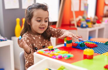 Adorable hispanic girl playing with construction blocks sitting on table at kindergarten