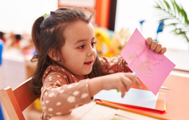 Adorable hispanic girl student smiling confident cutting paper at kindergarten