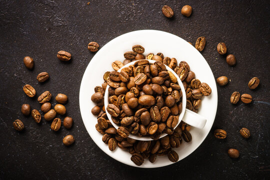 Coffee cup. Roasted coffee beans in white cup at dark table. Top view image.