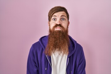 Caucasian man with long beard standing over pink background puffing cheeks with funny face. mouth inflated with air, crazy expression.
