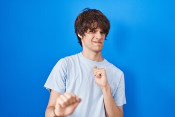 Hispanic young man standing over blue background disgusted expression, displeased and fearful doing...