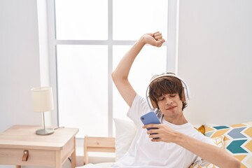 Young blond man listening to music sitting on bed at bedroom