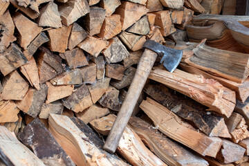 The stacked lumber lies in the woodpile. Axe with wooden handle