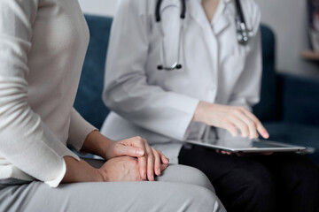 Doctor and patient sitting at sofa in clinic office. The focus is on female woman's hands, close up. Medicine concept