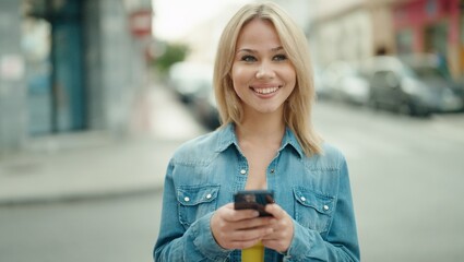 Young blonde woman smiling confident using smartphone at street