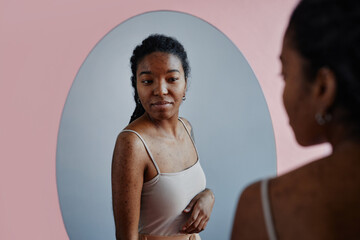 Candid young black woman with acne scars looking in mirror and smiling