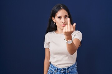 Young hispanic woman standing over blue background showing middle finger, impolite and rude fuck...
