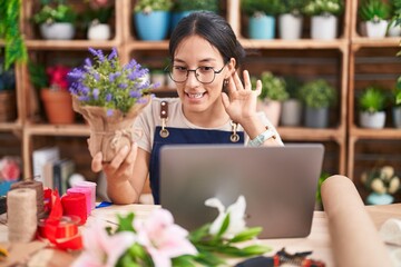 Young hispanic woman working at florist shop doing video call smiling with hand over ear listening an hearing to rumor or gossip. deafness concept.