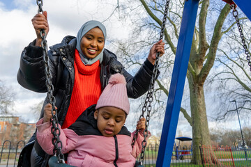 Mother swinging daughter (2-3) in playground