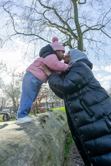 Fototapeta na wymiar Mother kissing daughter (2-3) standing on log in park