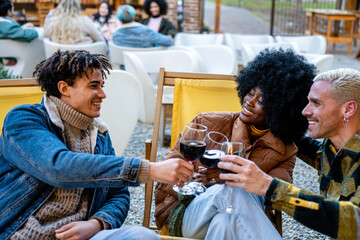Three friends sitting on deck chairs toasting together with glasses of red wine