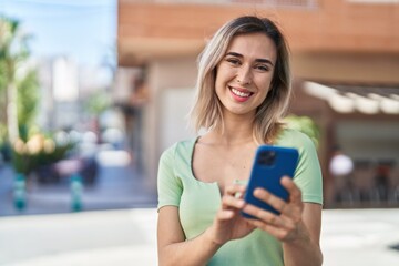 Young woman smiling confident using smartphone at street