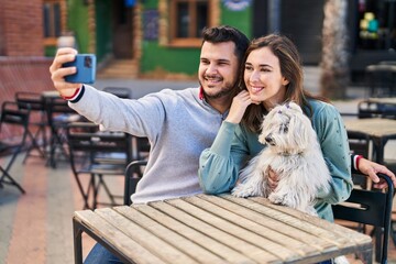 Man and woman holding dog making selfie by the smartphone at coffee shop terrace