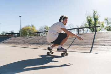 Energetic skater riding longboard in squat pose listening to music on headphones
