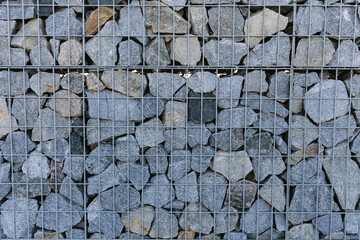 The crushed stone is fixed in the mesh. A fence made of natural stone, crushed stone, granite. Close-up. Texture