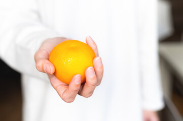 girl in a white sweater holds a fresh sweet tangerine against the background of herself in defocus. Close-up