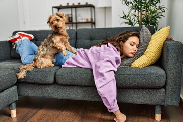 Young beautiful hispanic woman lying on sofa sleeping with dog at home