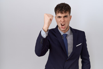 Young hispanic business man wearing suit and tie angry and mad raising fist frustrated and furious while shouting with anger. rage and aggressive concept.