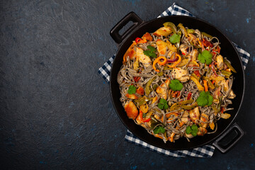 Wheat noodles with black sesame, fried in a wok with chicken and vegetables. Top view.