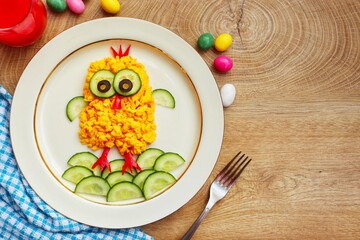 Scrambled egg easter chick made it from scrambled eggs,cucumbers,black olives and red hot peppers on plate with wooden background.Art food idea for kids Easter's breakfast.Top view.Copy space