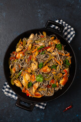 Wheat noodles with black sesame, fried in a wok with chicken and vegetables. Top view.