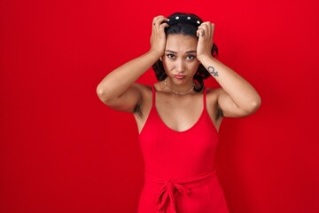 Young hispanic woman standing over red background suffering from headache desperate and stressed because pain and migraine. hands on head.