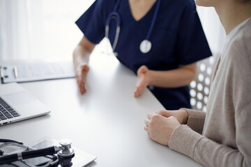 Doctor and patient sitting at the table in clinic while discussing something. The focus is on female patient's hands, close up. Medicine concept