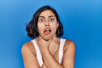 Young hispanic woman standing over blue background shouting and suffocate because painful strangle....