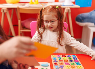 Fototapeta premium Adorable redhead girl playing with maths puzzle game sitting on table at kindergarten