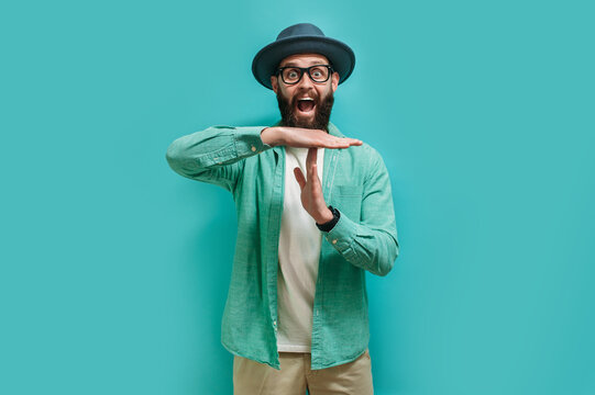 Young bearded hipster guy showing time out tired from work. Indoor studio shot against a blue background.