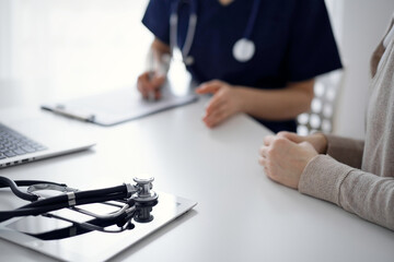 Stethoscope lying on the tablet computer in front of a doctor and patient at the background. Medicine, healthcare concept