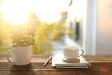 white tea cup and Verbena plant pot and notebook diary wooden table balcony with natural sunlight