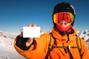 Snowboarder or skier holding blank lift pass in hand, portrait with mountain in the background. Ski...