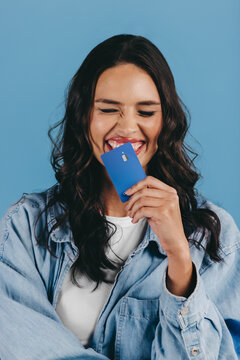New generation of banking: Excited gen z woman holds a credit card over her chin in a studio