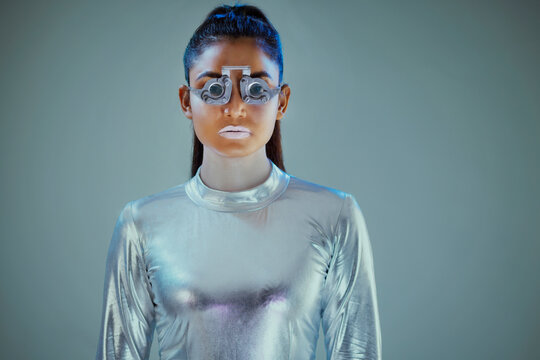  Model dressed as a  silver robot with eye prosthesis looking at camera on grey background