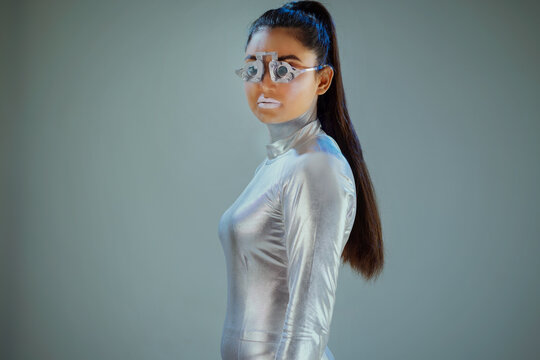 Side view of silver robot with eye prosthesis looking at camera on grey background