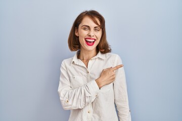 Young beautiful woman standing casual over blue background cheerful with a smile of face pointing with hand and finger up to the side with happy and natural expression on face