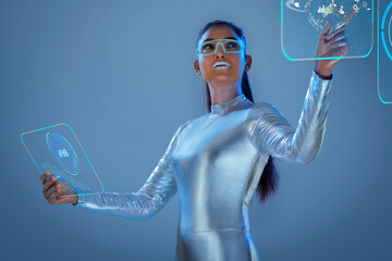 A model dressed as a robot wearing silver, futuristic  clothes holding a virtual  tablet, with virtual icons . A future technology concept