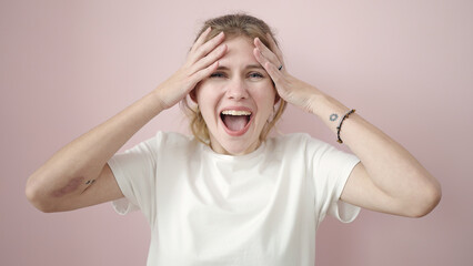 Young blonde woman standing with surprise expression over isolated pink background