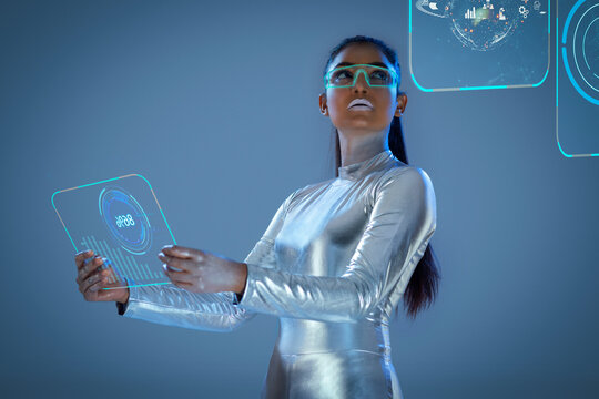 A model dressed as a robot wearing silver, futuristic  clothes holding a virtual  tablet, with virtual icons . A future technology concept