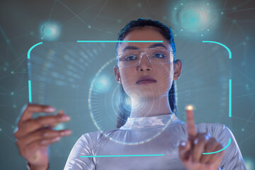 A woman wearing silver futuristic  clothes holding virtual tablet, with virtual icons in the background. A future technology concept