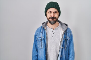Young hispanic man with tattoos wearing wool cap puffing cheeks with funny face. mouth inflated with air, crazy expression.