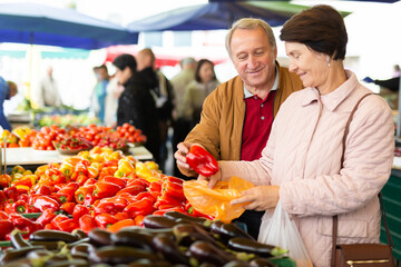 Aged man and woman customers buying pepper in open-air market