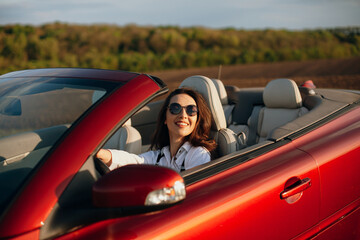 happy young beautiful woman in a white shirt sitting in a red car cabriolet with a white interior....
