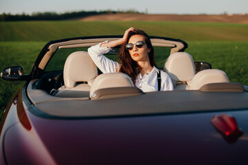 young beautiful woman in a white shirt sitting in a red car cabriolet with a white interior. red...